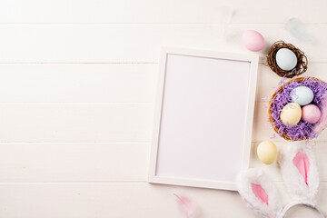 Fototapeta na wymiar White frame with easter decorations flat lay on beige background