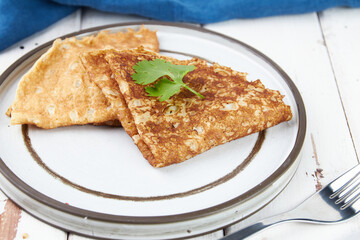 Crepes stuffed on plate, thin pancakes, blini, white wooden table