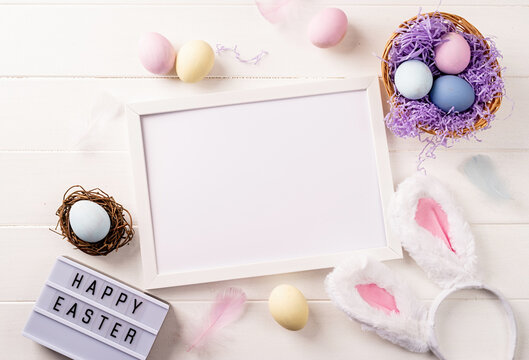 White frame with easter decorations flat lay on beige background