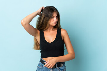 Young caucasian woman isolated on blue background having doubts while scratching head