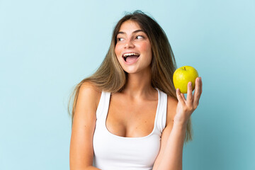 Young caucasian woman isolated on blue background with an apple and happy
