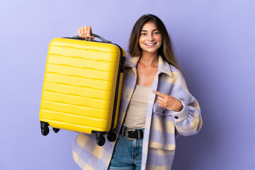 Young caucasian woman isolated on purple background in vacation with travel suitcase