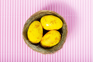 Yellow easter eggs in nest on a pink background. Minimal Easter concept. Top view. Copy space