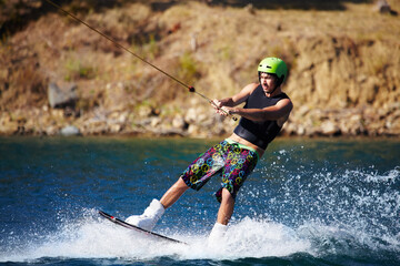 A young man wearing a helmut and lifejacket wakeboarding on a lake. A young man wearing a helmet and lifejacket wakeboarding on a lake.