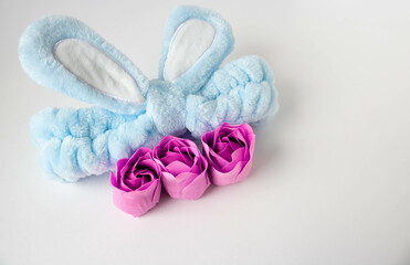 Obraz na płótnie Canvas A blue headband with rabbit ears and pink soap roses. Body care. Easter concept. Place for your text