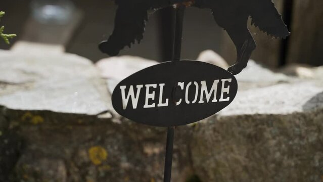 Welcome black metal plate in front of stone fence on metal rod with laser-cut letters . Sign with inscription in yard of the house. 