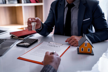 The real estate agent's home is handing over the house keys to the customer after the insurance contract is signed and explaining to the client at the office. Home Loan and Insurance Concepts