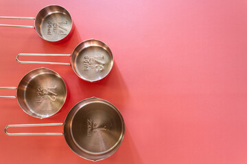 Collection of empty copper measuring cups on red background in top view