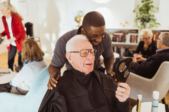 Smiling male nurse and elderly man looking in mirror at retirement home