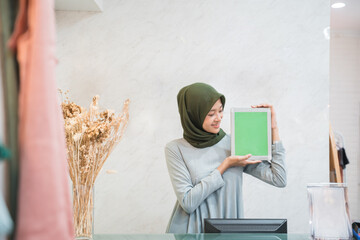 muslim fashion shop owner standing as a cashier holding a tablet pc