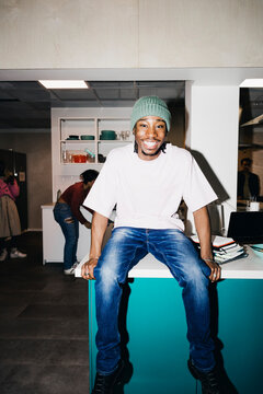 Portrait of happy young man sitting on dining table in kitchen at college dorm
