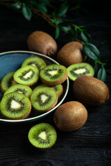 Close up look on kiwi fruit on the ceramic plate on the wooden background and green leaves 