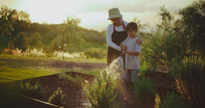 Grandmother and young grandson spending quality time together in the garden, watering garden beds at sunset