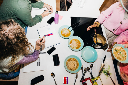 High angle view of multiracial young friends having noodles while studying at dining table in college dorm