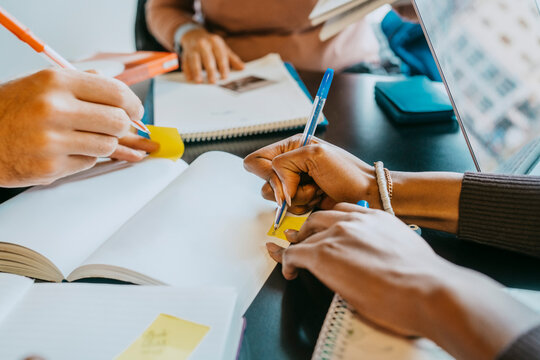Hands of university students writing in book at cafeteria
