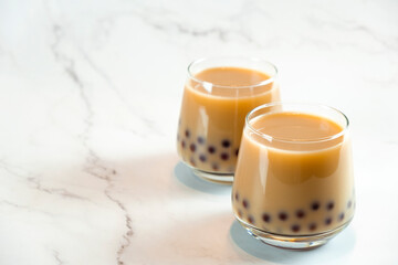 Two glasses with milk bubble tea with delicious tapioca pearls on marble background. Famous Taiwan milk jelly tea. Trendy drinks with copy space.