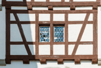 Brown wooden half-timbered wall with white walls and stained glass window in the middle. Beautiful historical piece of wall of building in Swiss old town on sunny summer day