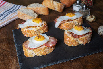 Slice of bread with bacon and grilled quail egg,on a wooden table.