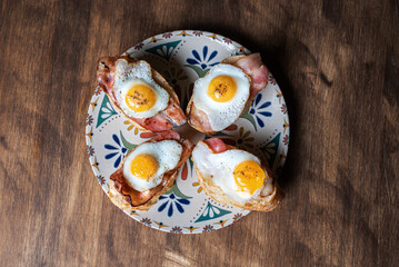 Slice of bread with bacon and grilled quail egg,on a wooden table.
