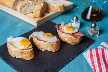 Slice of bread with bacon and grilled quail egg,on a wooden table.