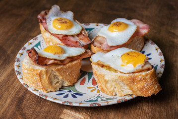 Slice of bread with bacon and grilled quail egg,on a wooden table.