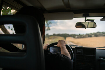 Young man driving a four wheel drive car in the countryside, driver inside the cabin of a car 4x4 , driving on an unsealed road, rural landscape in Spain © Alba