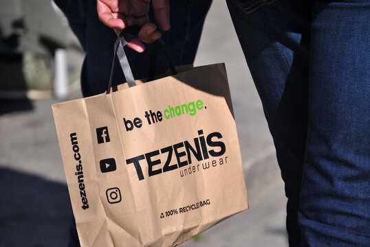 Pessoa a andar na rua com um saco de papel  na mão da marca de vestuário internacional, simbologia de sociedade consumismo