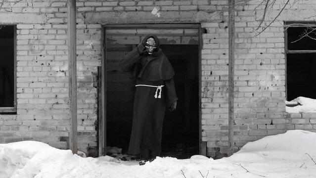 Grim Reaper Waving Hand by an Abandoned Old Brick Building in Winter Day. Slow Motion. Black and White (Monochrome) Toning