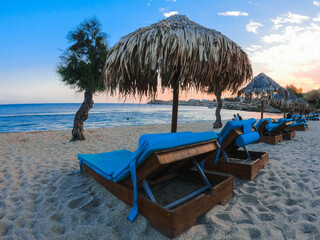 Vue de la plage paradisiaque de Mykonos en Grèce avec un transat et un parasol sous un coucher de...