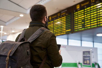 Young man with backpack in airport looking flight timetable