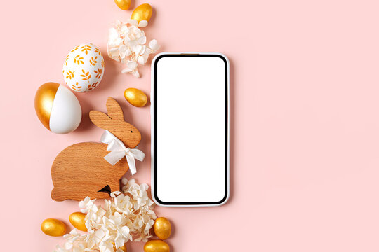 Smartphone mockup with Easter golden eggs, candy and flowers  on pastel pink background. Holiday concept. Happy Easter