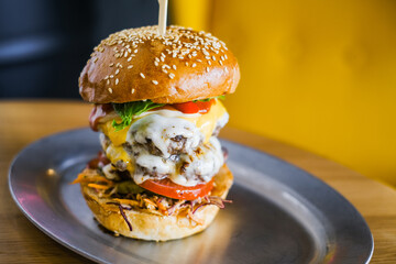 Big fat burger on a metal tray on a background of a yellow armchair