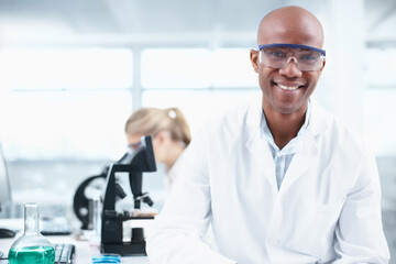 Smiling researcher. Portrait of a smiling young chemist in the lab with a female coworker in the background.