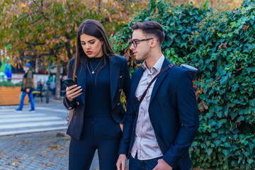 Business man and woman holding mobile phone and talking standing on the streets