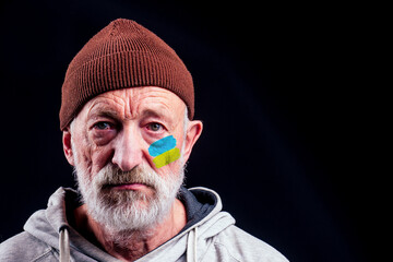 poor caucasian old men with Ukraine flag painted on cheek in studio black background. Russian versus Ukraine trade third world war disputes and anctions policy concept