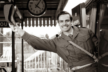Handsome male British soldier in WW2 vintage uniform at train station leaning out of train window,...