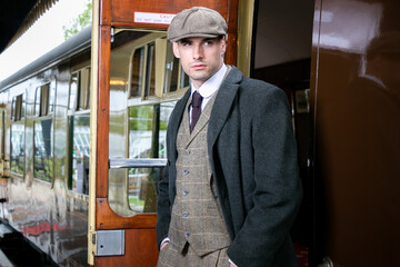 Handsome English male gangster at station leaving train looking at camera - obrazy, fototapety, plakaty