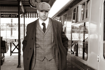Handsome English gangster with cigarette leaving train at railway station.