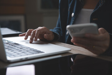 Closeup of business woman using mobile smart phone and working on laptop computer with digital tablet on office table at home
