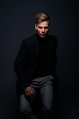 Formally dressed man with sharp jawline in his 20's posing in a studio in front of a black background.