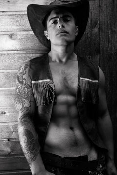 Handsome cowboy looking at camera wearing hat with open waistcoat revealing defined pecs and sixpack abs