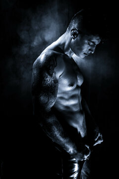 Moody low key portrait of attractive semi naked man with muscular body, pecs and defined abs