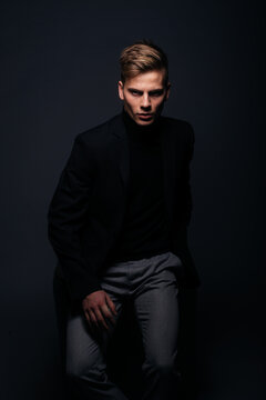 Formally dressed man with sharp jawline in his 20's posing in a studio in front of a black background.