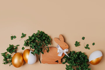 Obraz na płótnie Canvas Easter Bunny and golden eggs with green flowers on beige background. Holiday concept. Happy Easter card.