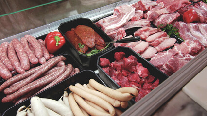 meat department display shelves with selection of typical fresh raw meats slices and variety of sausage products inside market or supermarket refrigerated background.