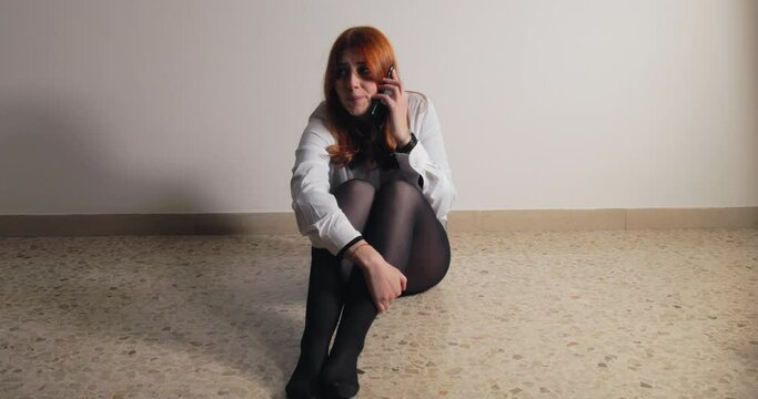 Girl sitting on the ground talking on the phone scared of the abuser in house