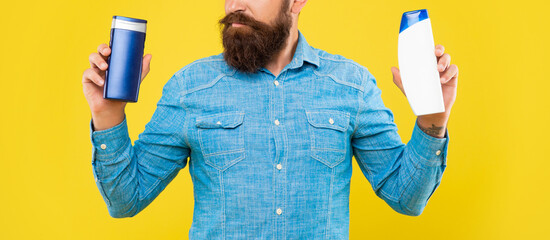 cropped brutal bearded man choose shampoo bottle on yellow background, haircare