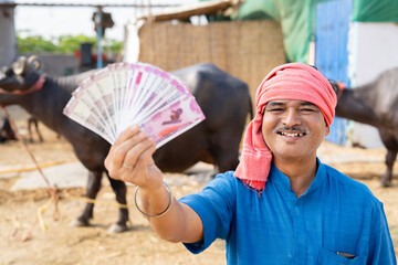 Confident milk dairy farmer showing indian currency money by looking at camera - concept of...