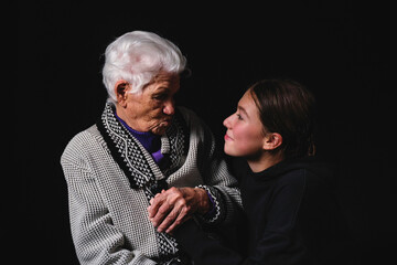 Elderly woman sitting with an adult granddaughter a black background.