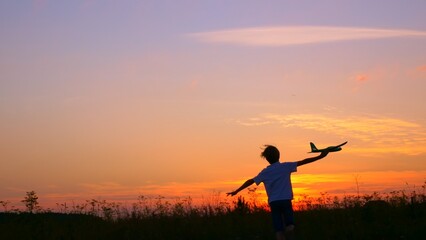 A boy at sunset runs across the field in his hands an airplane, the Kid dreams of becoming an astronaut pilot. Childhood dream to run with a toy. Pilot of a children's plane. Dream concept